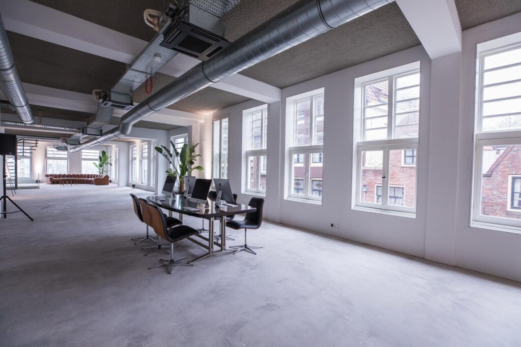 Ruime, moderne kantoorruimte aan de Prins Hendrikkade met grote ramen, industriële details en een vergadertafel met iMacs.